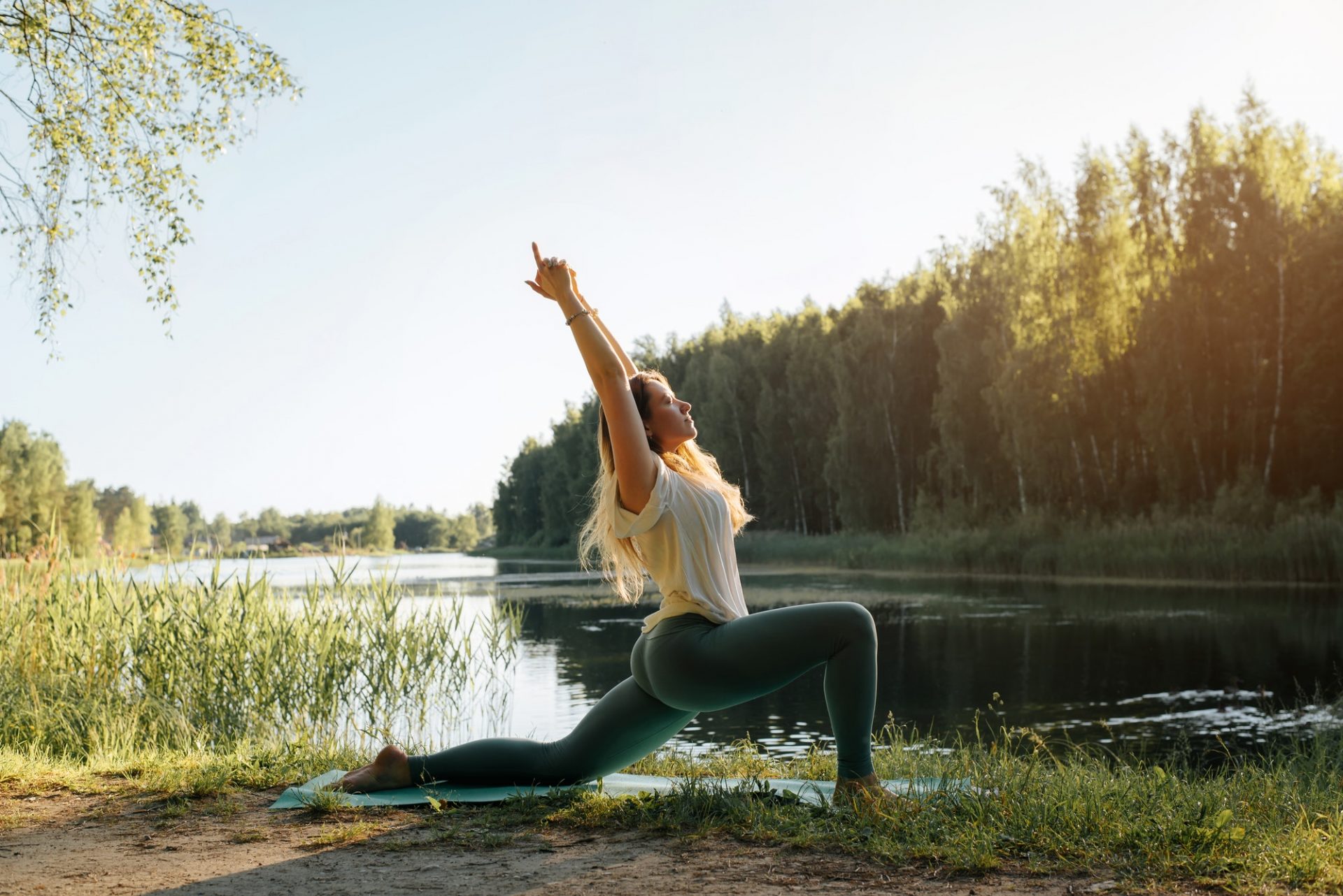 Yoga in nature. Young woman practicing yoga on lake at sunset, summer. Fitness model standing on