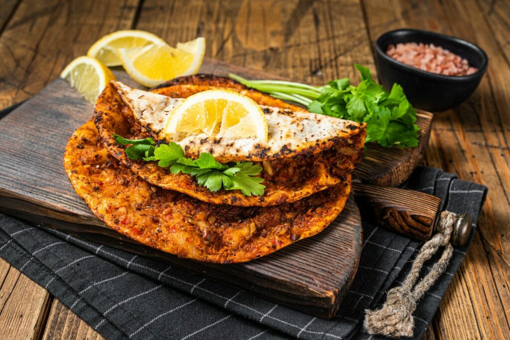 Turkish cuisine made with thin dough and minced beef meat lahmacun on wooden board with herbs