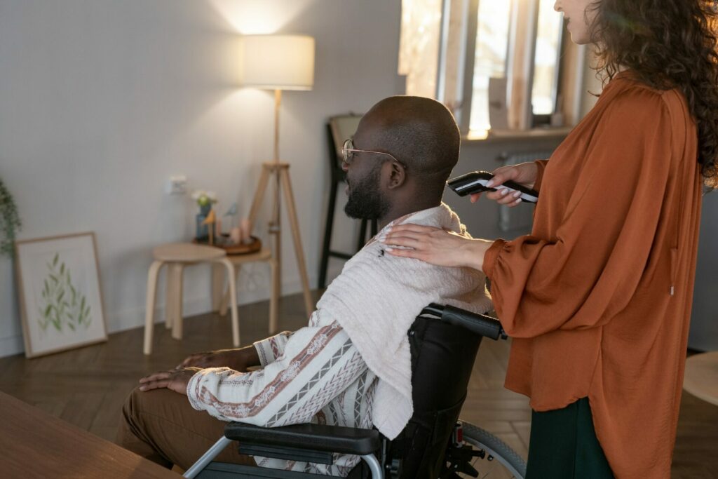 Man with disability having his hair cut by electric trimmer held by caregiver
