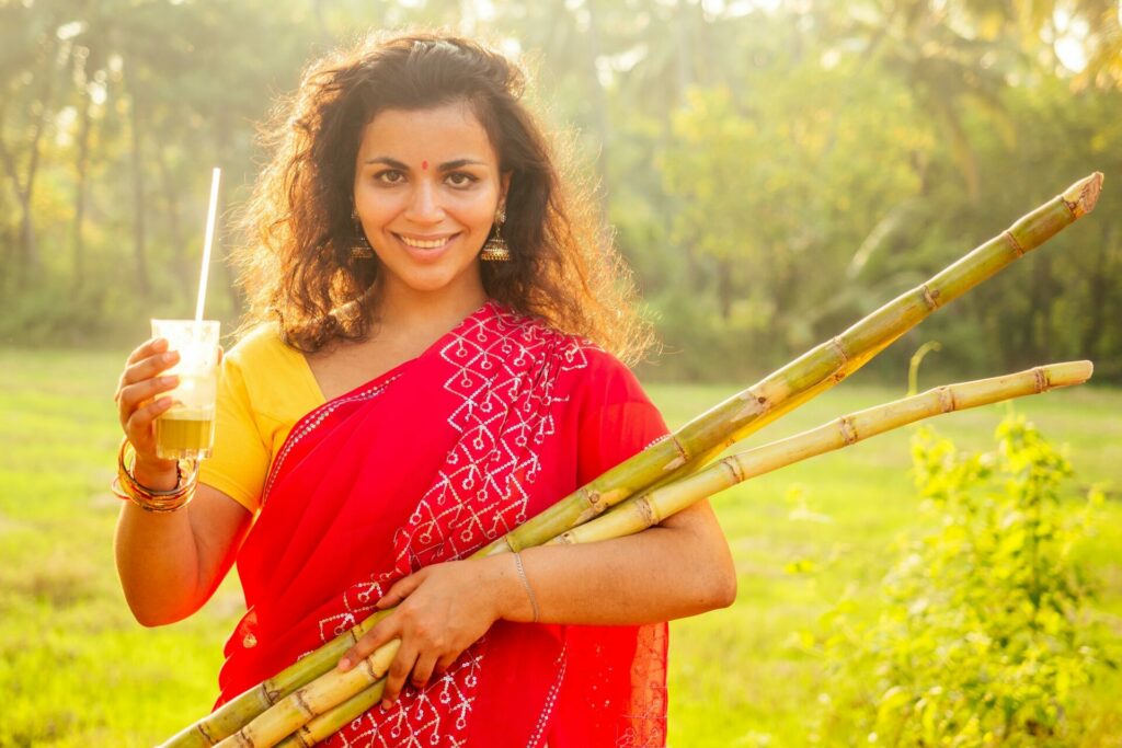 beautuful induan woman in red sari standing near sugarcane juice maker apparatus machine