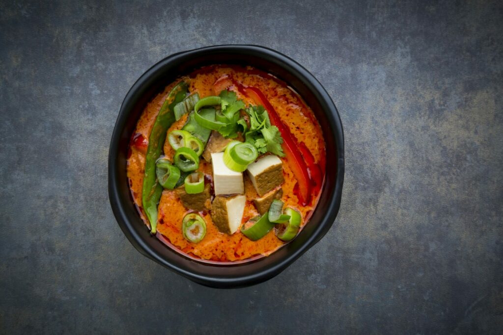 Bowl of red Thai Curry with snow peas, carrots, bell pepper, spring onions and smoked tofu