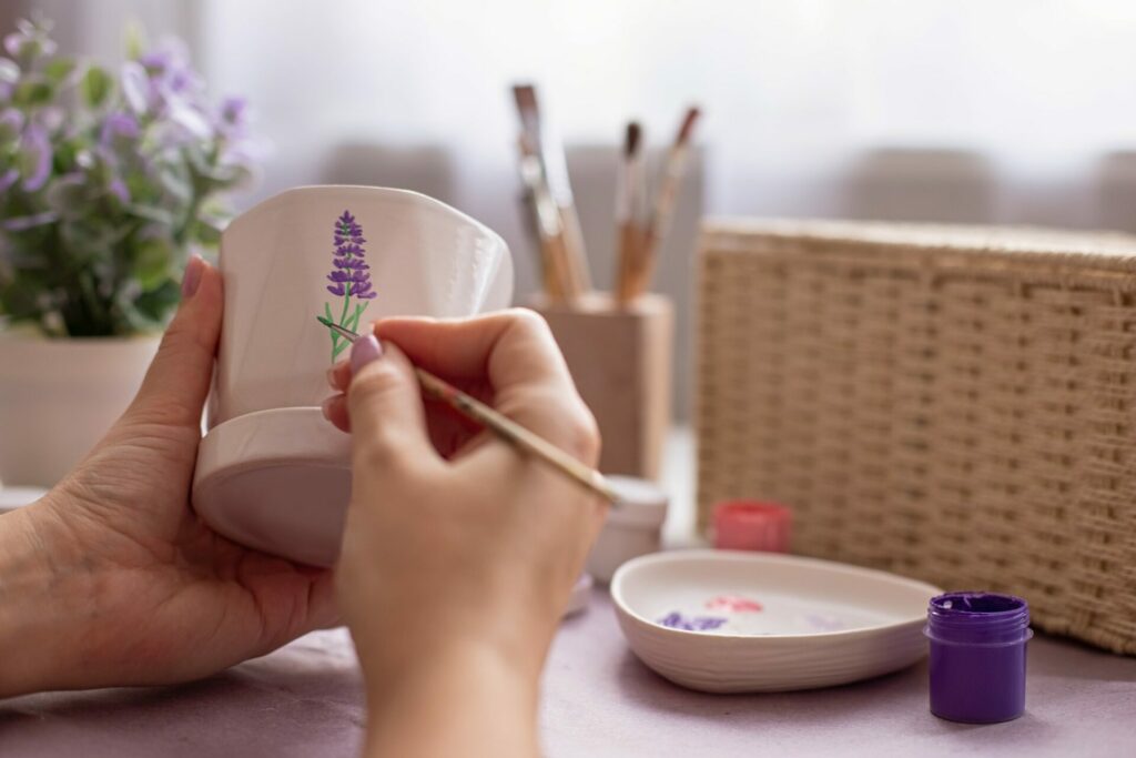 Girl's hands draw a lavender flower on a white ceramic pot