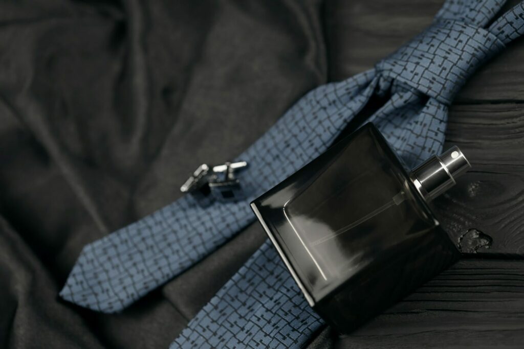 A bottle of luxury men's perfume and cufflinks with blue tie lie on a black fabric background