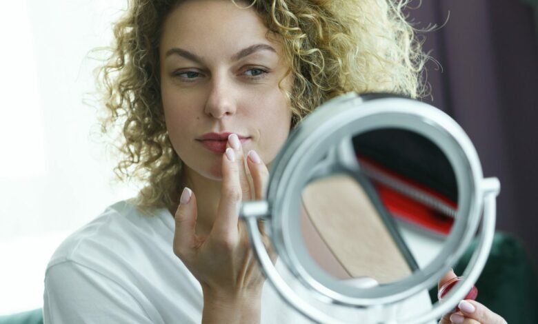 Beautiful woman looking into a mirror and applying lip oil