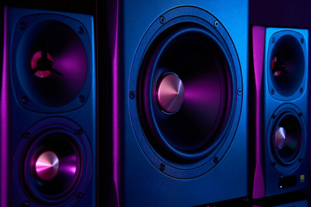 Two sound speakers and subwoofer on dark background with neon lights