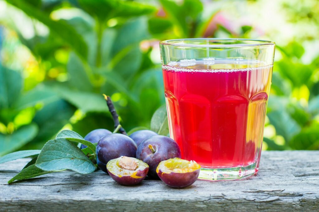 Plum and prunes juice in glass on wooden table background. Natural Green Leaf